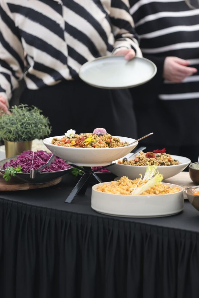 A buffet setup with diverse dishes, attended by people in striped outfits.